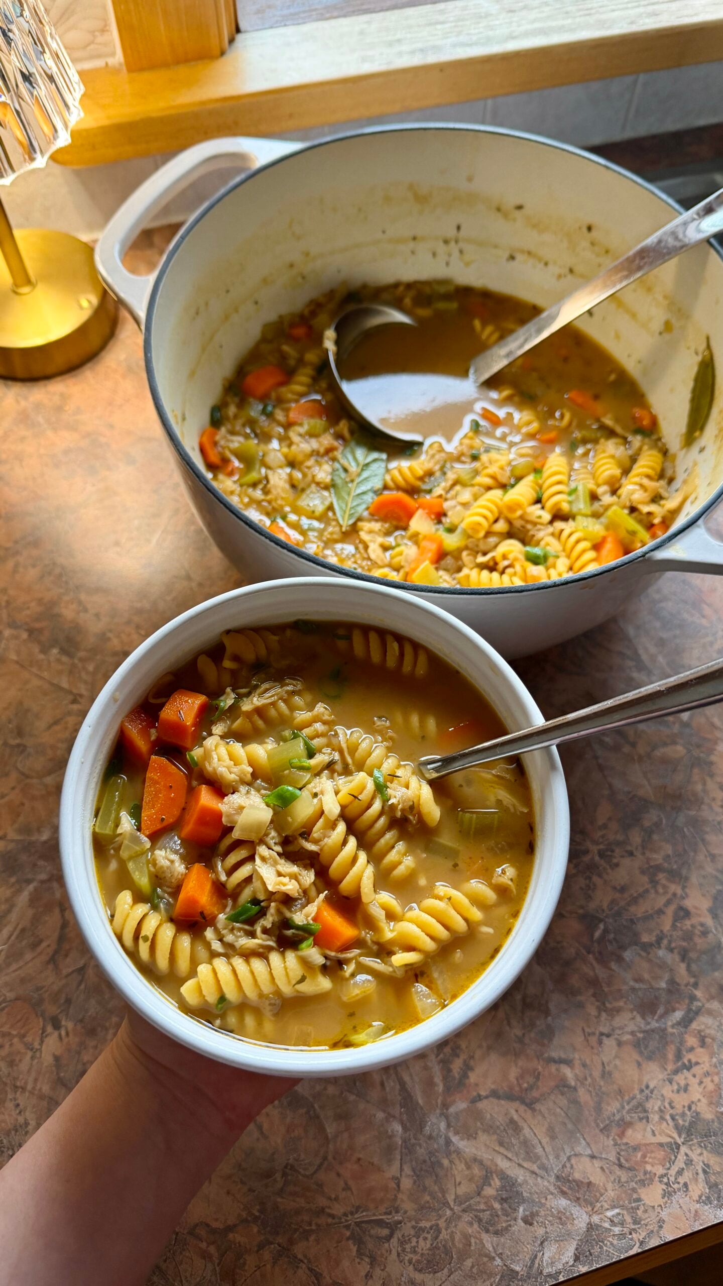 a bowl of vegan chicken noodle soup with the full pot of soup in the background