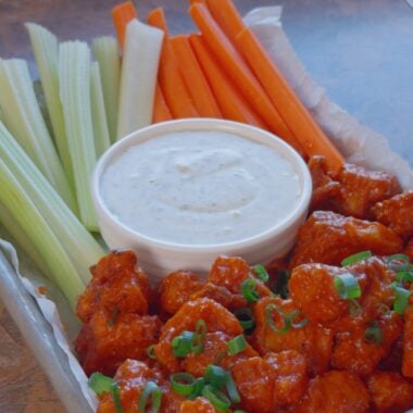 air-fryer buffalo tofu on a serving tray with ranch, carrot sticks, and celery sticks, topped with sliced scallions
