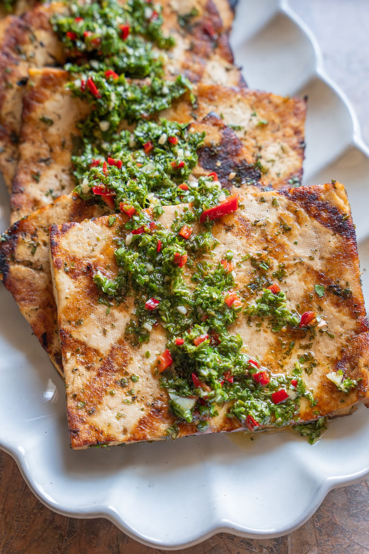 steaks of grilled tofu lined up on a plate and topped with chimichurri