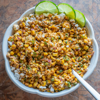 a bowl of vegan street corn salad with slices of lime as garnish
