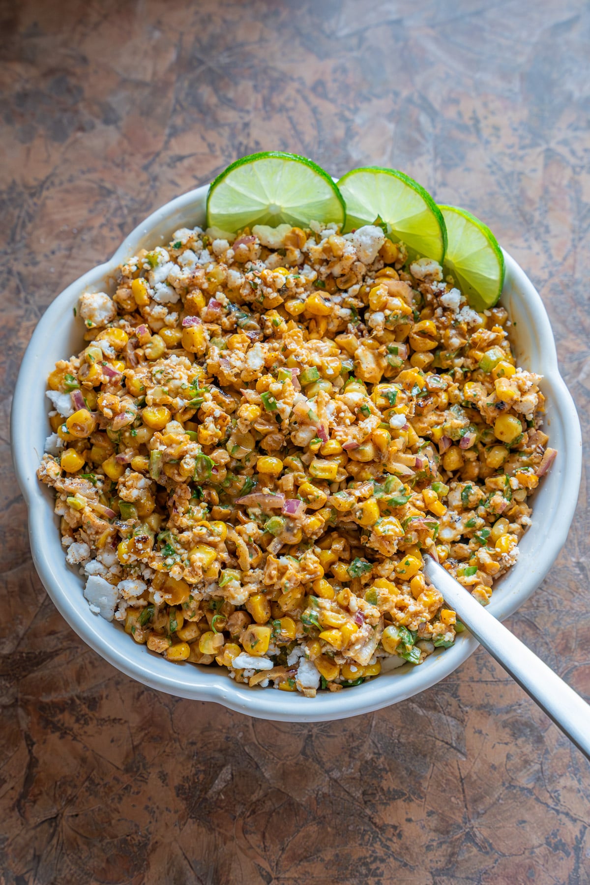 a bowl of vegan street corn salad with slices of lime as garnish