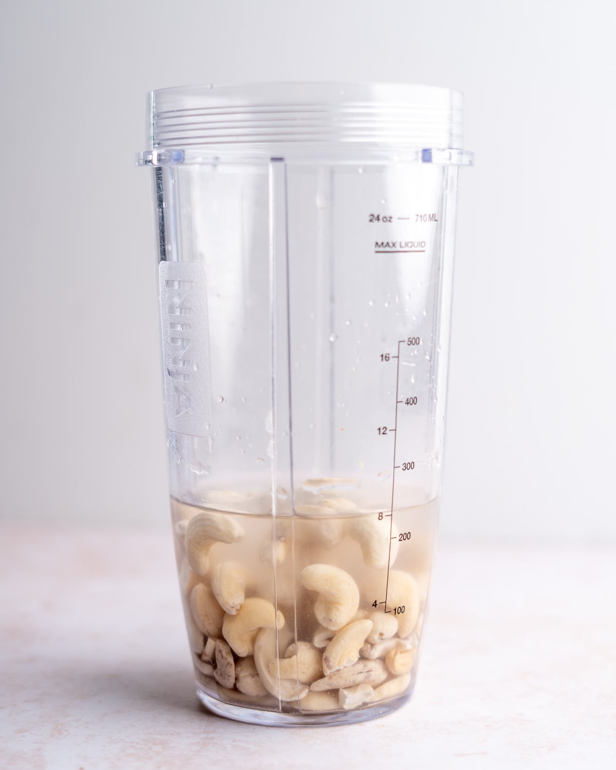 A blender cup with raw cashews and water.