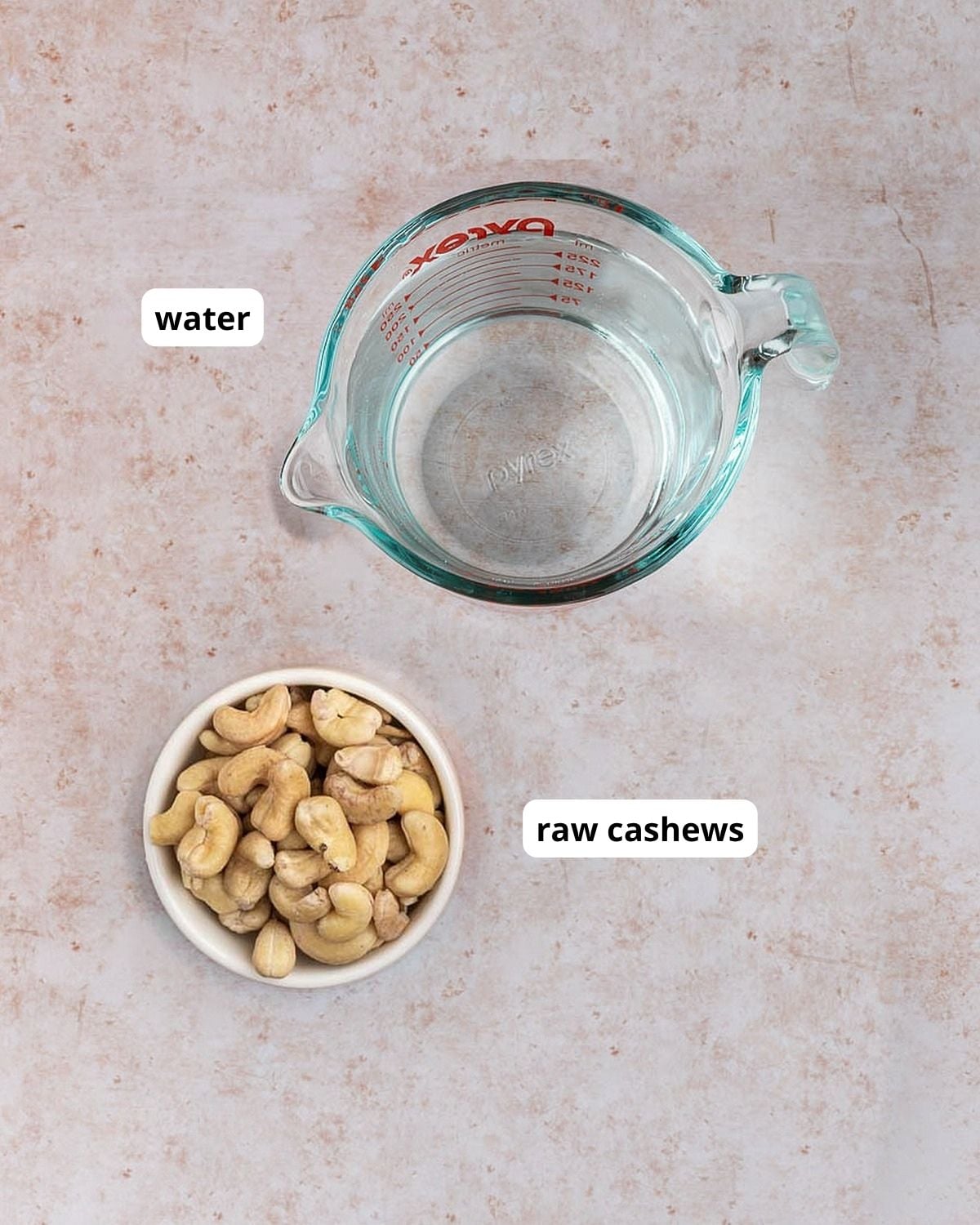 Overhead shot of a Pyrex measuring cup with water and a small white dish with raw cashews.