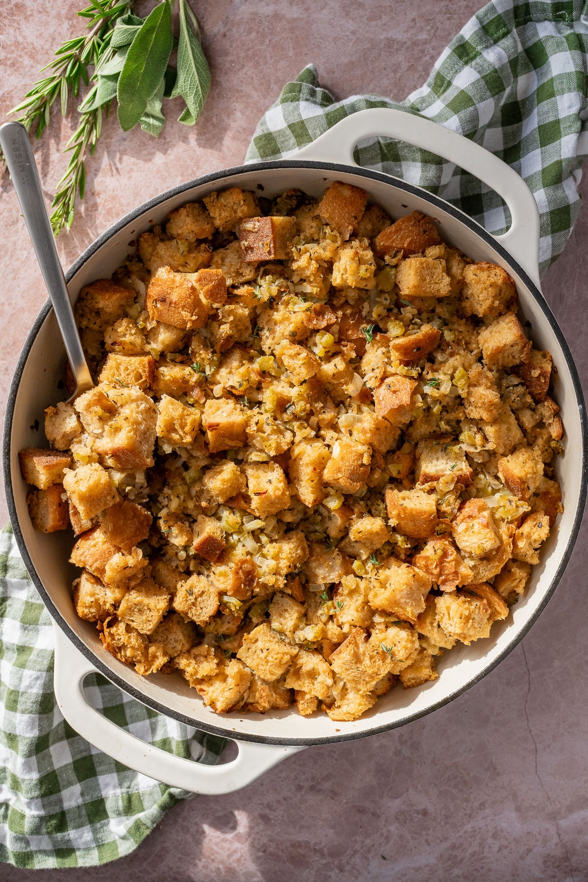 Classic vegan stuffing in a white braiser pan sitting on a green and white checkered towel.